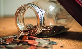 Glass of coins tipped on its side, spilling coins on table.