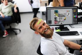 Man with beard in office setting, looking at camera.